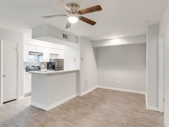 A room with a ceiling fan and a kitchen area in the background.