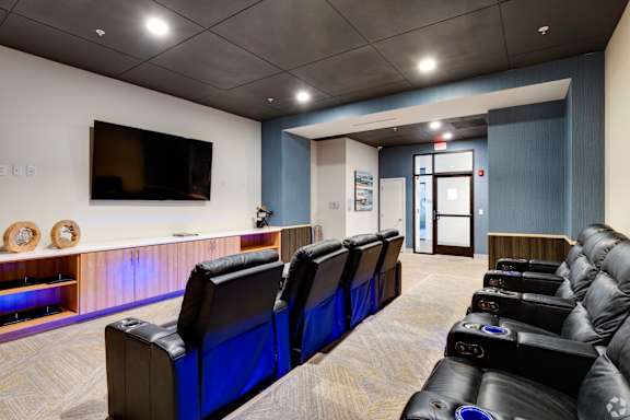 A row of black leather seats are arranged in a room with a television on the wall.