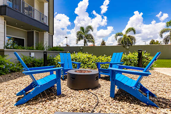 Two blue chairs and a table are on a gravel patio.