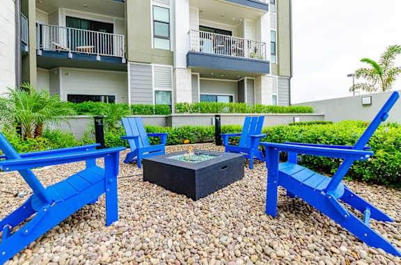 A fire pit surrounded by blue chairs and tables in front of a building.
