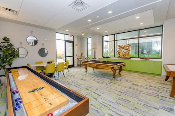 A shiny pool table is in the middle of a room with a green bench and yellow chairs.