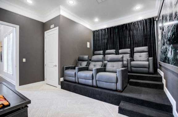 A home theater with a row of grey leather seats and a black carpet.