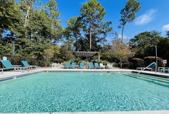 a swimming pool with blue chairs and trees in the background