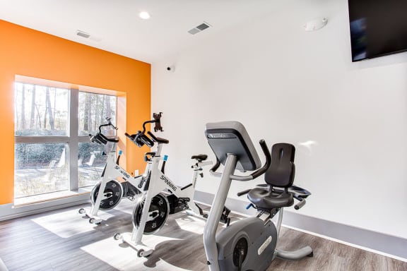 A home gym with orange walls and a television mounted on the wall at The Carter 4250 Apartments, Norcross, GA