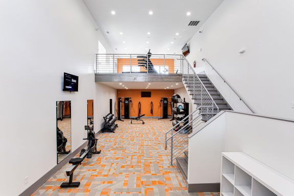 A gym with orange tiles on the floor and a staircase at The Carter 4250 Apartments, Norcross, 30093