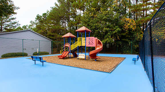 A playground with a blue surface and a red slide at Wildcreek Apartments, Clarkston, GA 30021