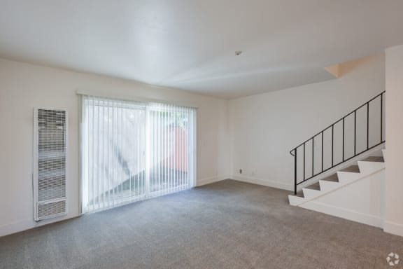 the living room of an empty house with a staircase and a large window