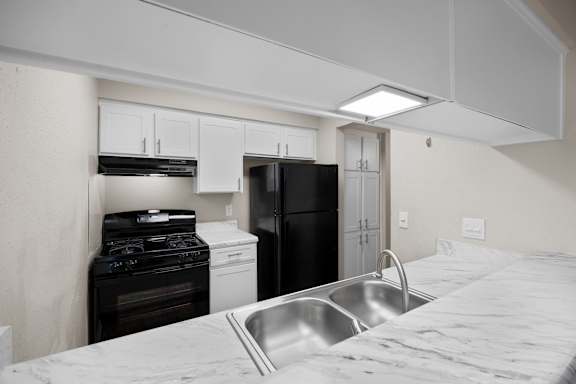 A kitchen with a black refrigerator, white oven, and a stainless steel sink.