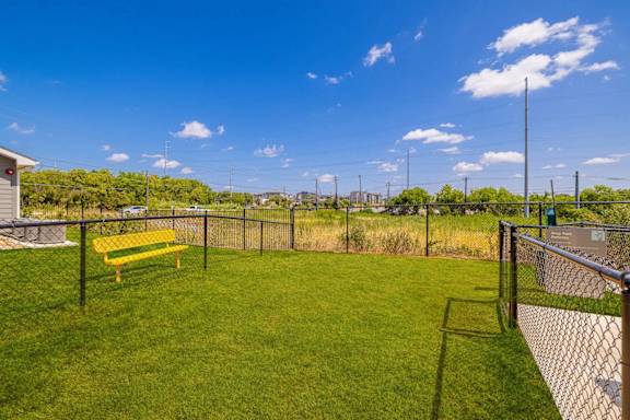 A yellow bench sits in a grassy field next to a chain link fence.