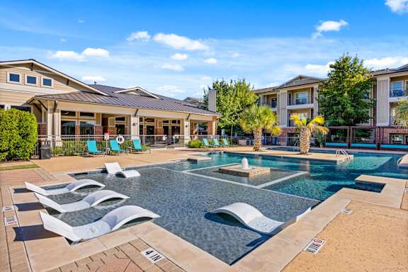 A swimming pool with a slide and a building in the background. at Bridge at Southpark Meadows, Austin, TX