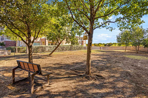 A park bench sits under a tree on a sunny day. at Bridge at Southpark Meadows, Texas, 78748