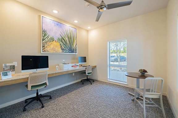A room with a desk, chairs, and a painting of a desert scene.