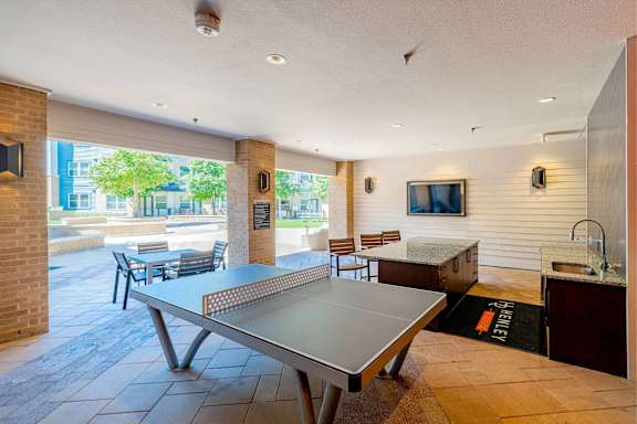 A ping pong table is in the middle of a room with a TV and a counter. at Bridge at Henley, Austin, TX