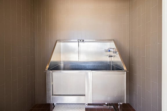 A stainless steel counter with a glass top is in a room with beige tiled walls.