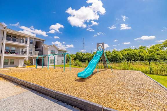 A playground with a blue slide in the foreground and apartment buildings in the background.