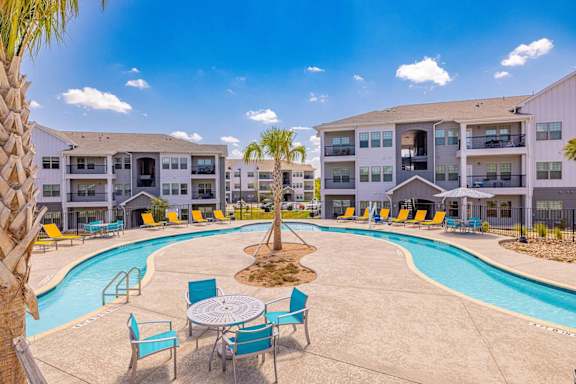 A pool area with chairs and a table in front of apartment buildings.