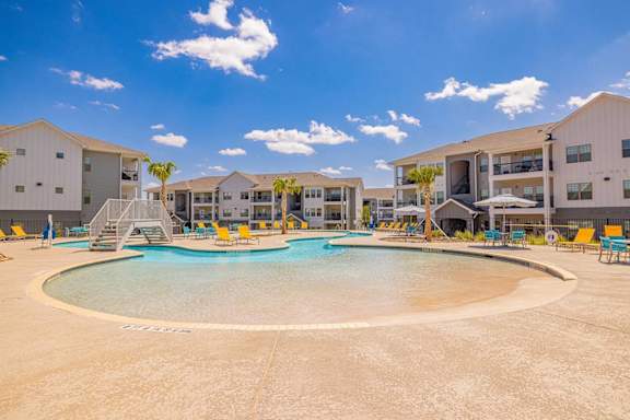 A large outdoor swimming pool surrounded by sun loungers and palm trees.
