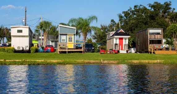 a row of tiny houses on a grassy area next to a body of water