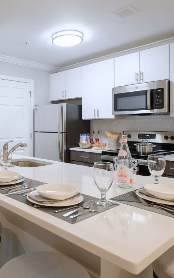 a kitchen with white cabinets and a white island with plates and glasses on it