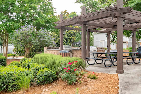 A wooden pergola with a sign on it is surrounded by greenery and a picnic table.