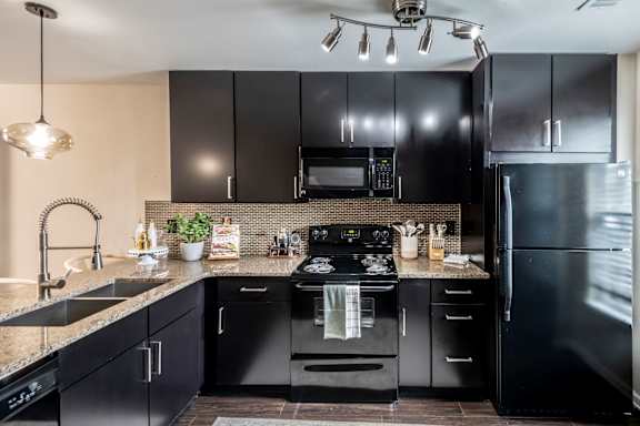 A black kitchen with a sink, stove, and refrigerator.