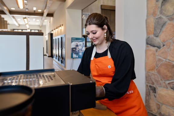 a woman in an orange apron standing at a registrar machine in a museum