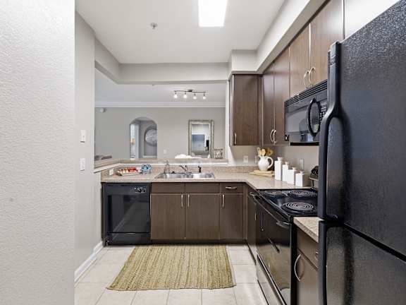 A kitchen with a black refrigerator and brown cabinets.