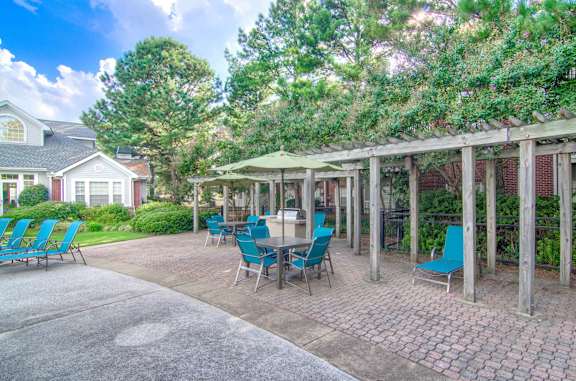 A patio with blue chairs and a table is surrounded by trees at Enclave at Wolfchase Apartments, Memphis