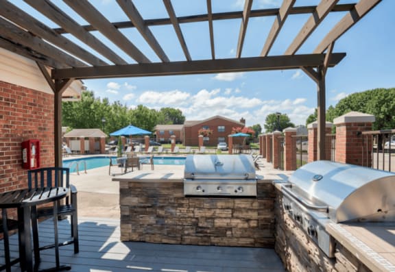 a patio with a grill and a swimming pool with umbrellas at Brightwaters Apartments, Little Rock