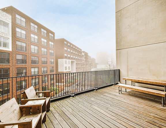 A wooden balcony with benches and a railing overlooks a cityscape.