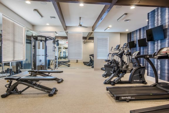 a gym with treadmills and other exercise equipments in a room with windows at The McKenzie Park Apartments, Little Rock, 72223