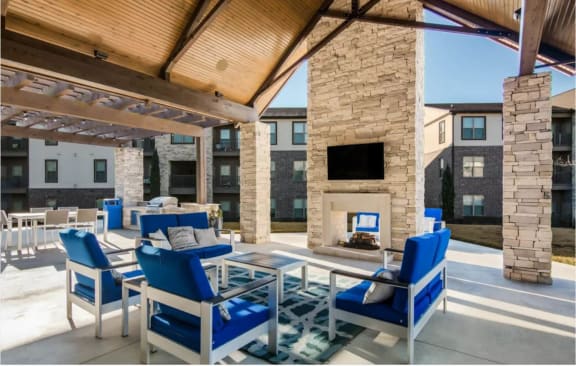 a covered patio with blue chairs and a fireplace at The McKenzie Park Apartments, Little Rock, AR 72223
