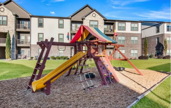 a playground with a swing set in front of an apartment building at The McKenzie Park Apartments, Arkansas, 72223