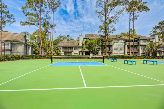A tennis court with a net and four blue benches.