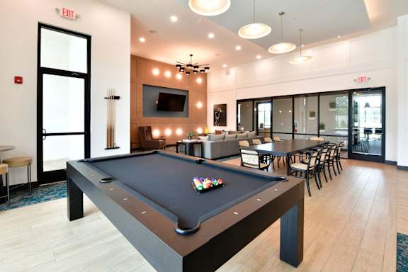 A pool table is in the middle of a room with a TV and chairs.
