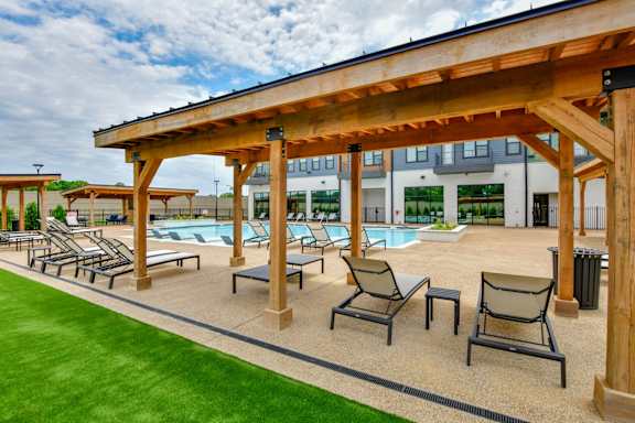 A wooden pergola over a pool area with lounge chairs.
