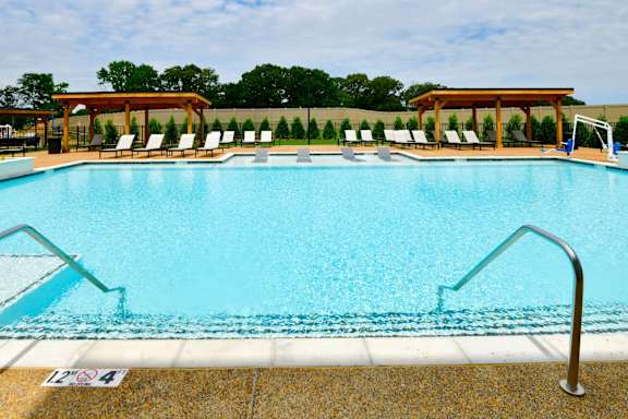 A swimming pool with a metal ladder and a poolside with chairs.