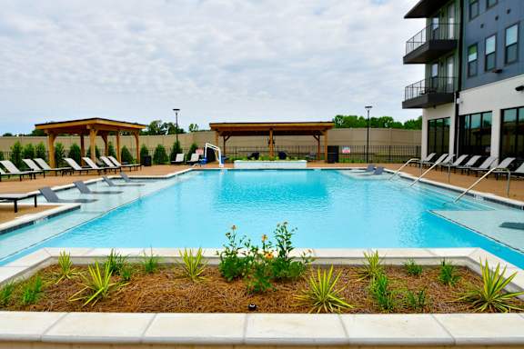 A large swimming pool surrounded by a concrete border and a small garden in the foreground.