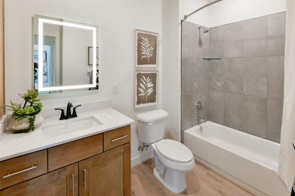 A bathroom with a back-lit mirror, bathtub, and toilet