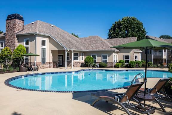 A swimming pool in front of a house with a green umbrella.