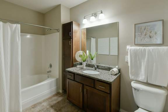 A bathroom with a white toilet, a white sink, a white shower curtain, and a brown vanity. at Hall Creek Apartment Homes, Arlington 38002