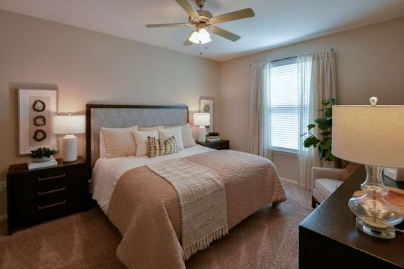 A bedroom with a large bed, a ceiling fan, and a nightstand with a lamp. at Hall Creek Apartment Homes, Arlington 38002