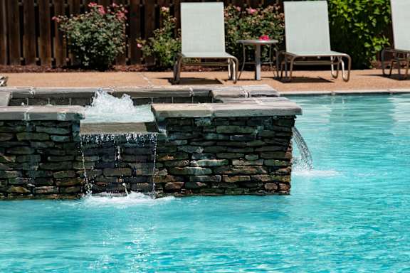 A pool with a waterfall and chairs around it. at Hall Creek Apartment Homes, Arlington