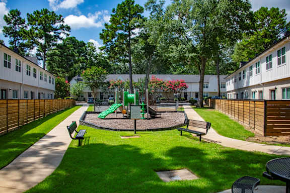 A playground with a green slide and a red flower bush.