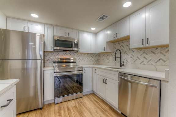 A kitchen with white cabinets and stainless steel appliances.at The Garden District Apartments, Germantown, TN 38138