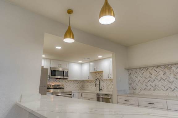 A modern kitchen with a white countertop and gold pendant lights.at The Garden District Apartments, Germantown, TN