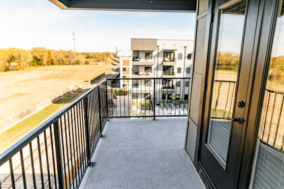 A balcony with a black railing and a view of a building and trees at Harbor Side at Conwood Flats Apartments in Uptown Memphis, TN