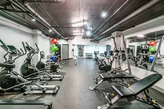 A gym with a row of treadmills and elliptical machines.