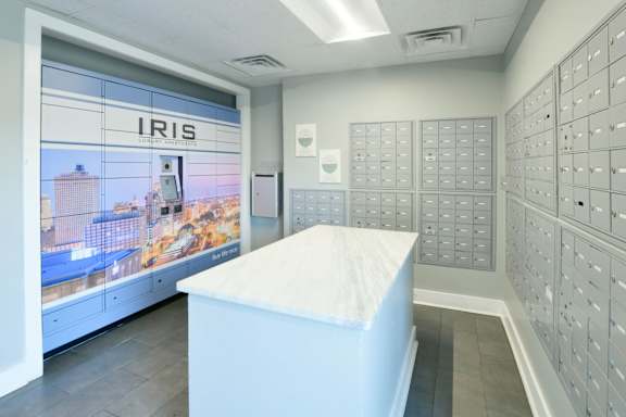 A white reception desk in front of a wall of mailboxes and a window showing a cityscape.