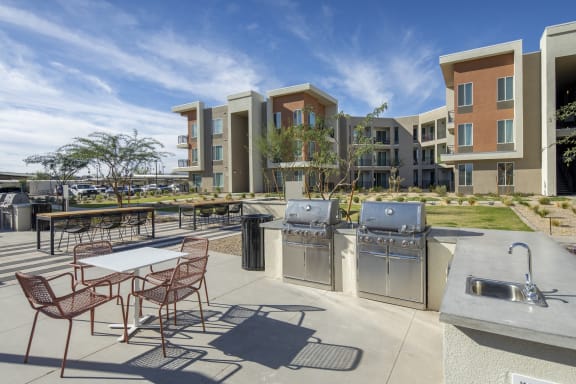 an outdoor patio with tables and barbecue grills and apartments in the background